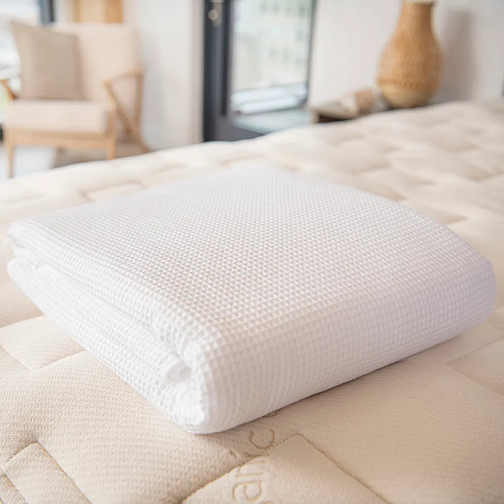 Bedroom view Naturepedic Organic Cotton Waffle Blankets in white folded on mattress